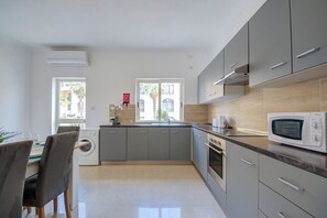 A modern kitchen with grey cabinets, a built-in oven, and a microwave. There is a window with a view of palm trees and a building outside. - Magnificent Minimal Apartment Close to Attractions (St. Julian's)