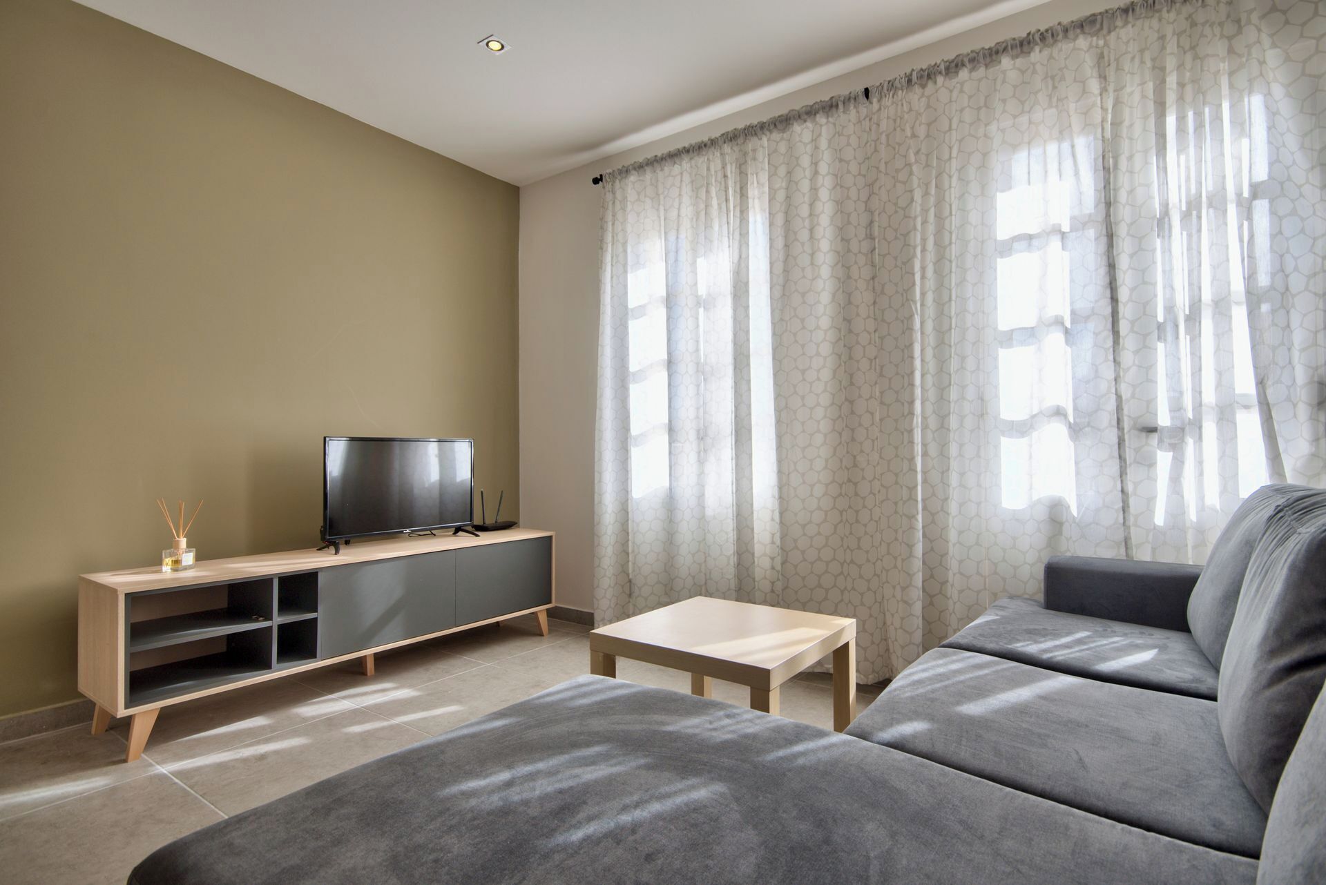 Ein modernes Wohnzimmer mit einem grauen Sofa, einem Fernseher auf einem Holzboden und einem kleinen Tisch.