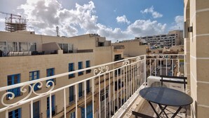 A balcony with a table and chairs, overlooking a residential area with multiple buildings and a construction crane in the background. - Amazing Airy Apartment Surrounded by All Amenities (Gzira)