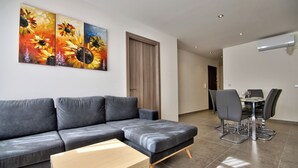 A modern living room with a grey sofa, a wooden coffee table, and a dining area with a table and chairs. - Amazing Airy Apartment Surrounded by All Amenities (Gzira)