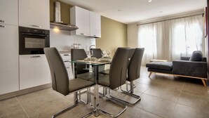 A modern kitchen with white cabinets, a built-in oven, and a dining area with a glass table and four chairs. - Amazing Airy Apartment Surrounded by All Amenities (Gzira)