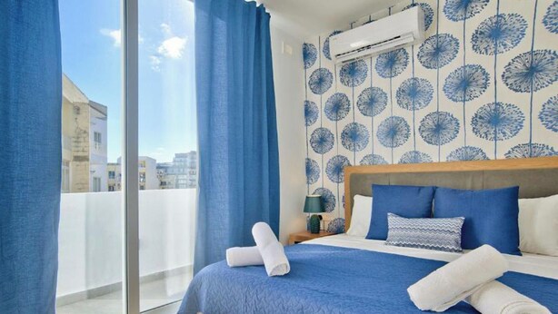 Quarto de hotel com uma cama grande, cabeceira de madeira, vista através de uma porta deslizante e parede com padrão.