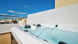 Uma banheira de hidromassagem no terraço com água cristalina, cercada por um edifício moderno com parede branca e vista para o horizonte da cidade.