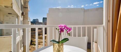 A balcony with a white table and a gold vase with pink flowers.