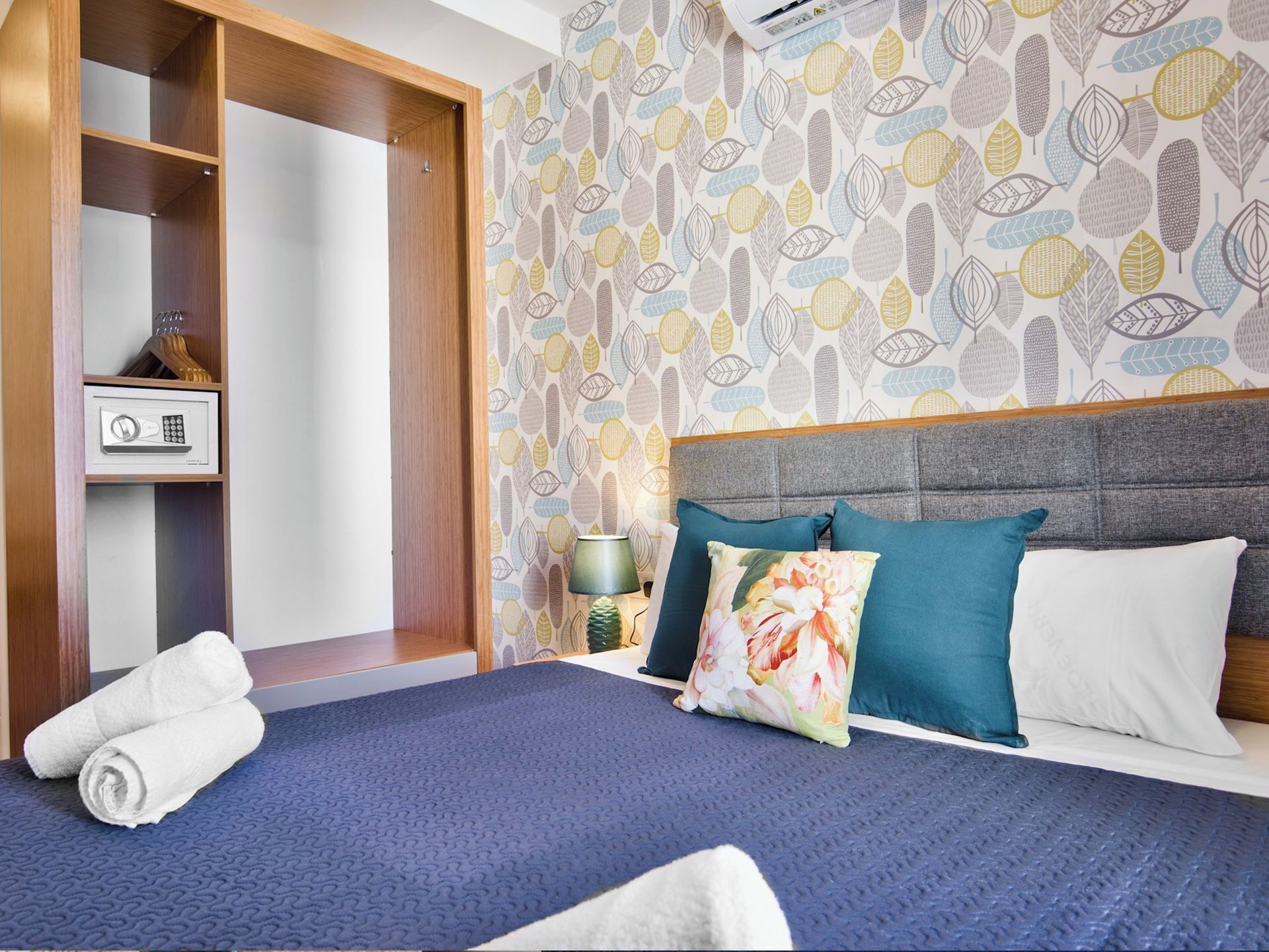 Une chambre d’hôtel avec un lit, une armoire et un mur recouvert d’un papier peint à motifs de feuilles.