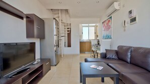 A modern living room with a flat-screen TV, a sofa, a coffee table, and a kitchen in the background. - Stunning City Views Sliema Duplex Penthouse (Sliema)