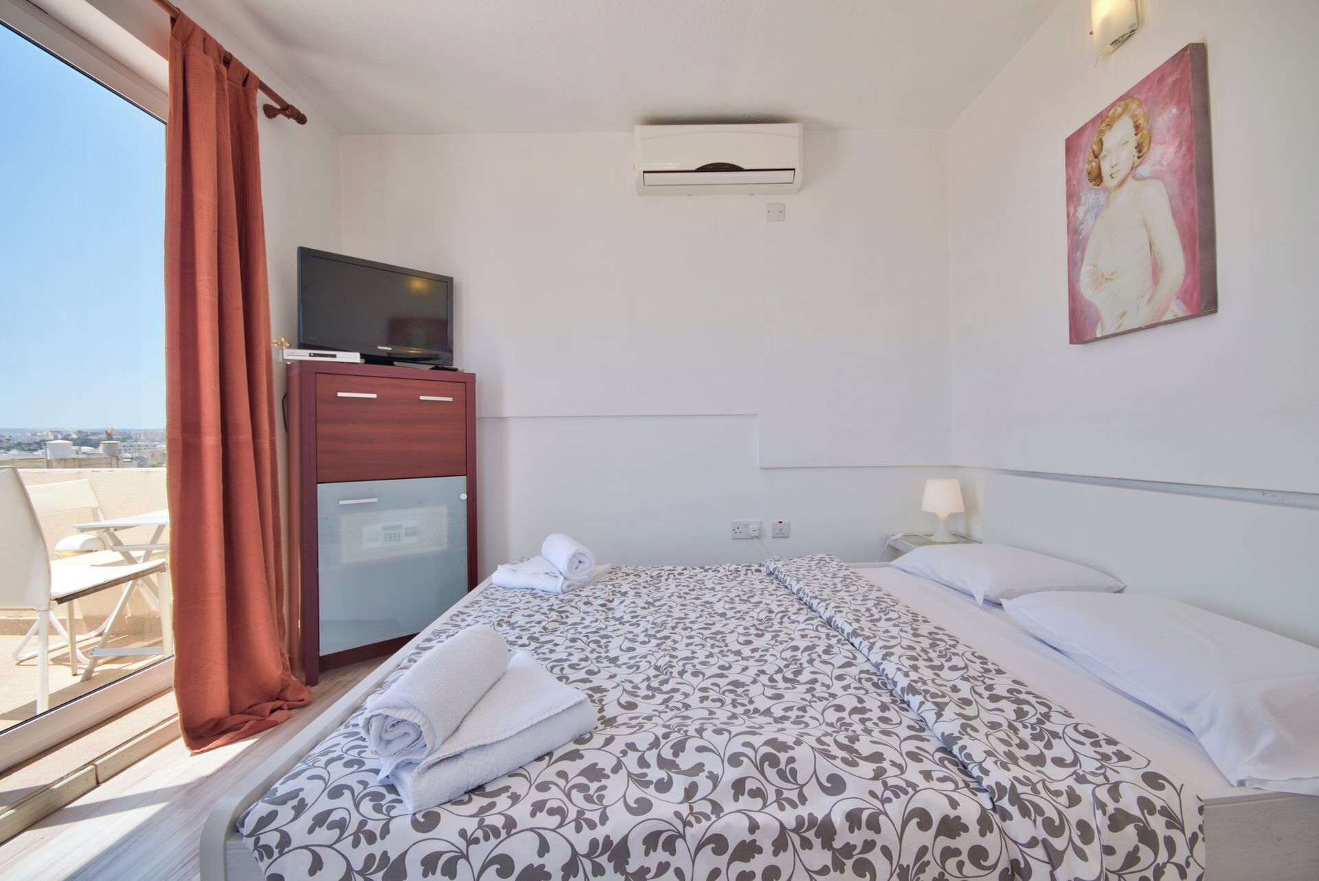 Et hotelværelse med en seng, et skrivebord med tv, en minibar og et billede på væggen.