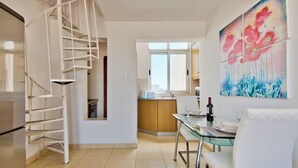 A modern kitchen with a spiral staircase, a dining area with a glass table and white chairs, and a vibrant floral painting on the wall. - Stunning City Views Sliema Duplex Penthouse (Sliema)