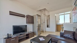 A modern living room with a flat-screen TV, a coffee table, a sofa, and a kitchen in the background. - Stunning City Views Sliema Duplex Penthouse (Sliema)