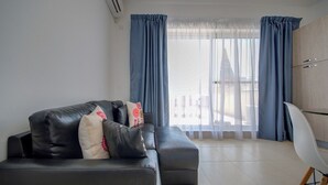 A modern living room with a black leather sofa, a white chair, and a wooden cabinet. - Off The Strand Gzira Top Floor Apartment (Gzira)