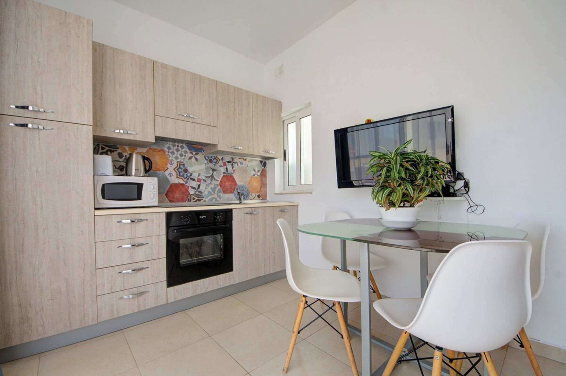 A modern kitchen with wooden cabinets, a microwave, an oven, and a dining area with a glass table and white chairs.