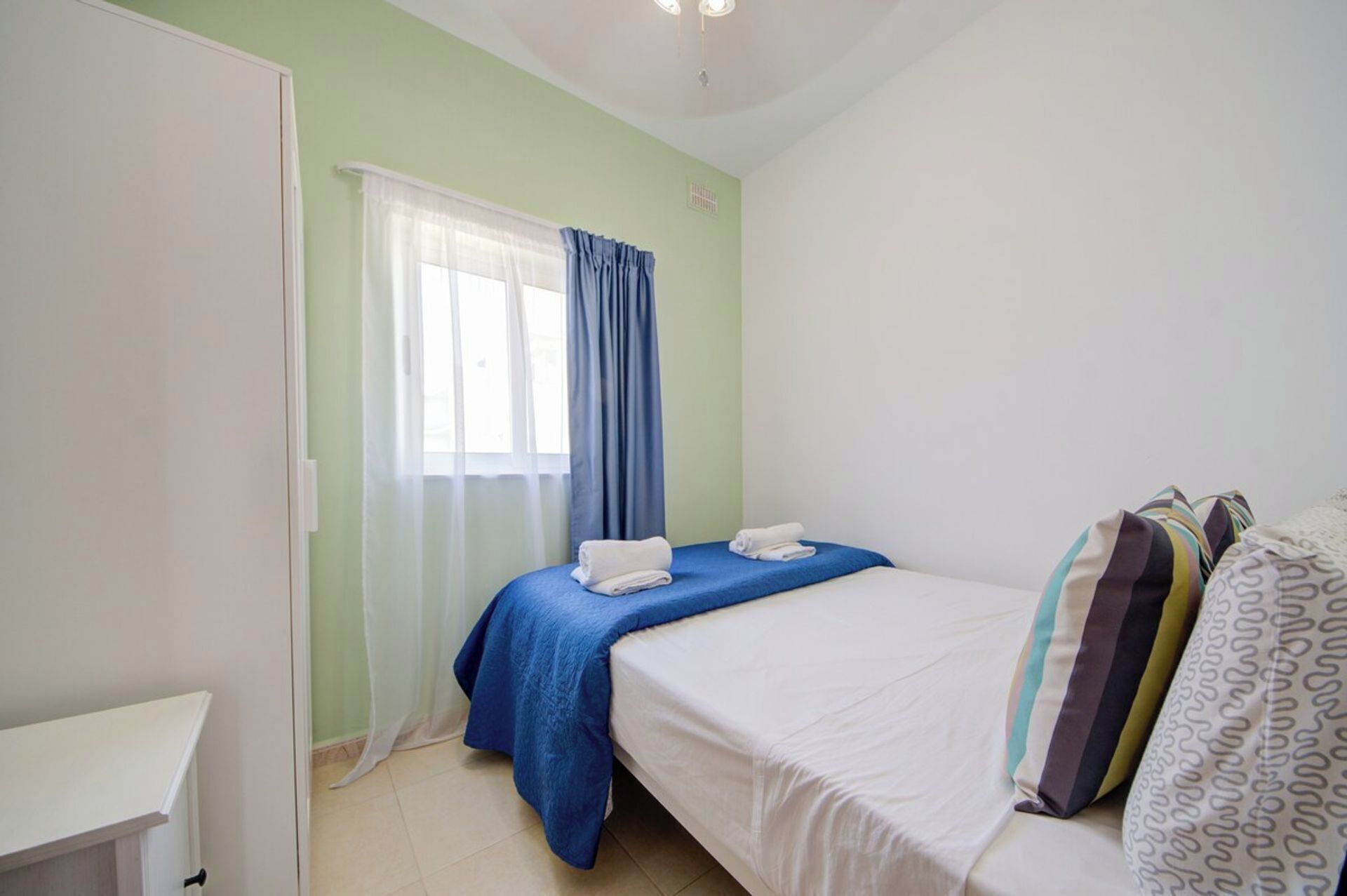 A bedroom with a bed, a nightstand, a window with curtains, and a door.