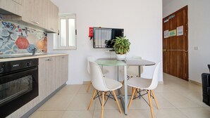 A modern kitchen with a dining area, featuring a built-in oven, a TV, and a potted plant. - Off The Strand Gzira Top Floor Apartment (Gzira)
