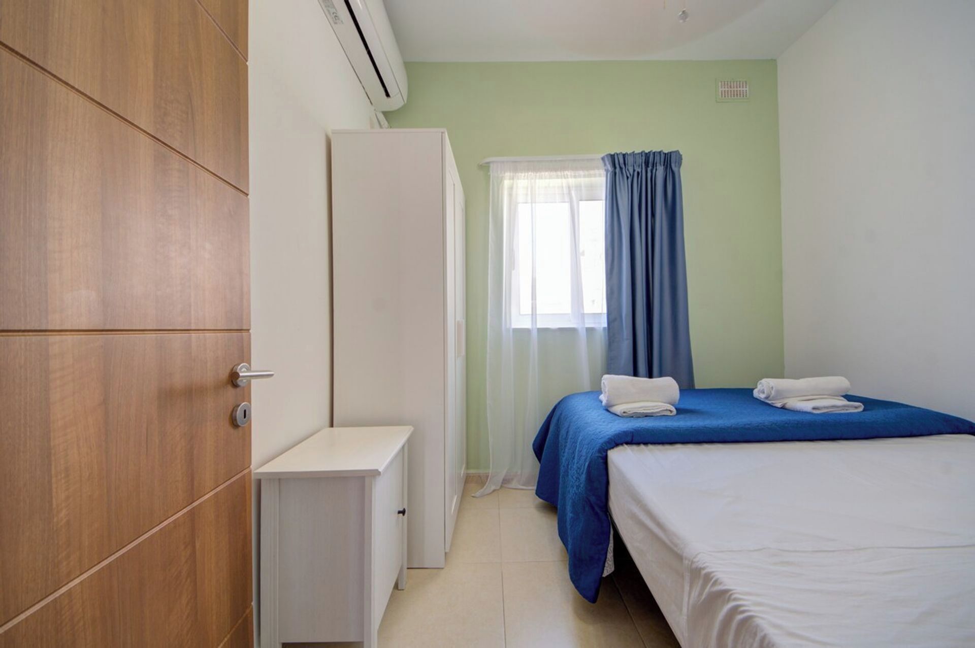 Ein Schlafzimmer mit einem Bett, einem Kleiderschrank, einem Nachttisch und einem Fenster mit Vorhängen.