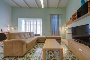 Un salon avec un canapé beige, une table basse en bois, un téléviseur posé sur un meuble en bois et des carreaux de sol à motifs.