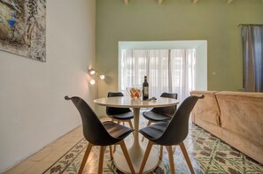 Un coin repas avec une table ronde, quatre chaises, une bouteille de vin et un vase rempli d’oranges.