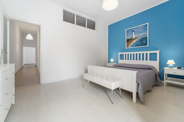 A bedroom with a bed, bench, bedside tables, and a painting on the wall.