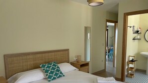 A neatly made bed with white linens and a teal pillow, a wooden nightstand with a lamp, and a bathroom visible through an open door. - Apartment with shared swimming pool, Sta. (Baiona)
