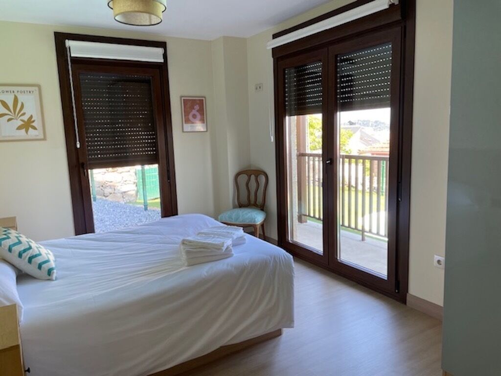 A bedroom with a bed, a chair, and a balcony with a view.