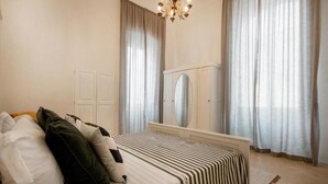 Een slaapkamer met een bed, een spiegel, gordijnen en een kroonluchter.