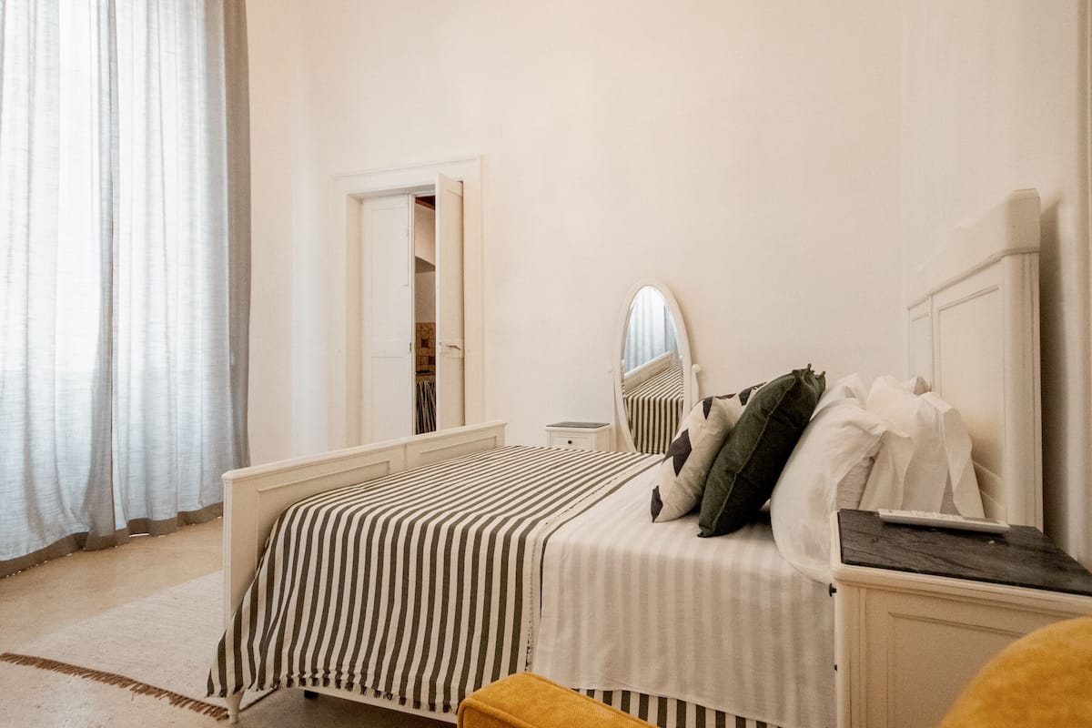Een slaapkamer met een bed, nachtkastje, spiegel en een deur naar een badkamer.