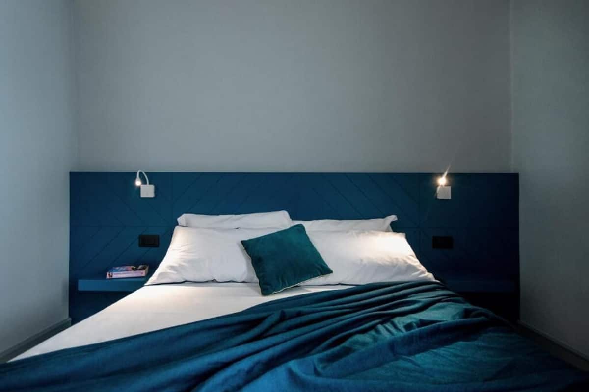Een bed met wit en turquoise beddengoed, een turquoise plaid en twee bedlampjes.