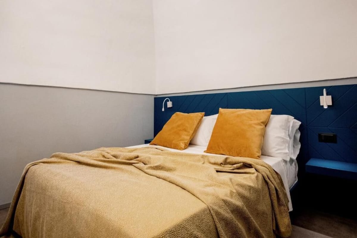 Een bed met een blauw hoofdeinde, twee kussens en een deken.
