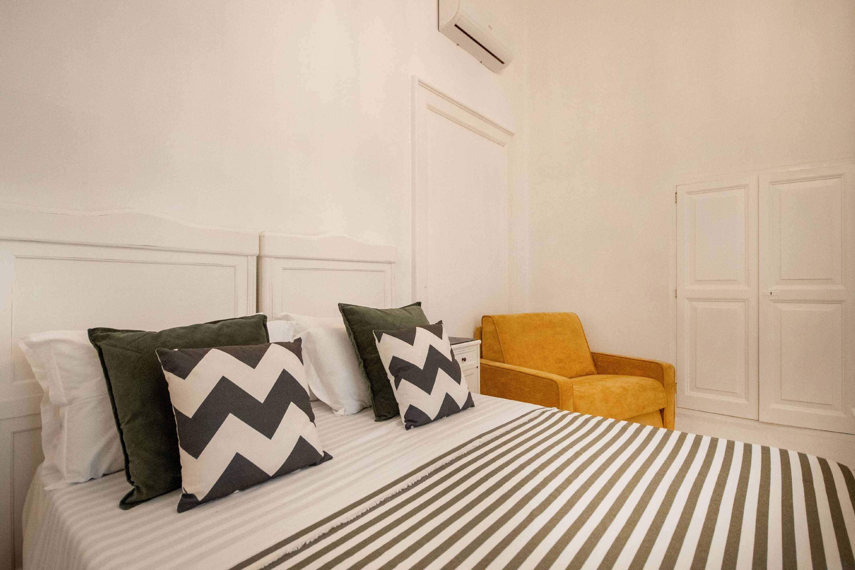 Una habitación de hotel con cama, almohadas, una silla y un armario.