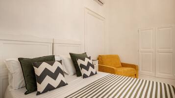 Una habitación de hotel con cama, almohadas, una silla y un armario.