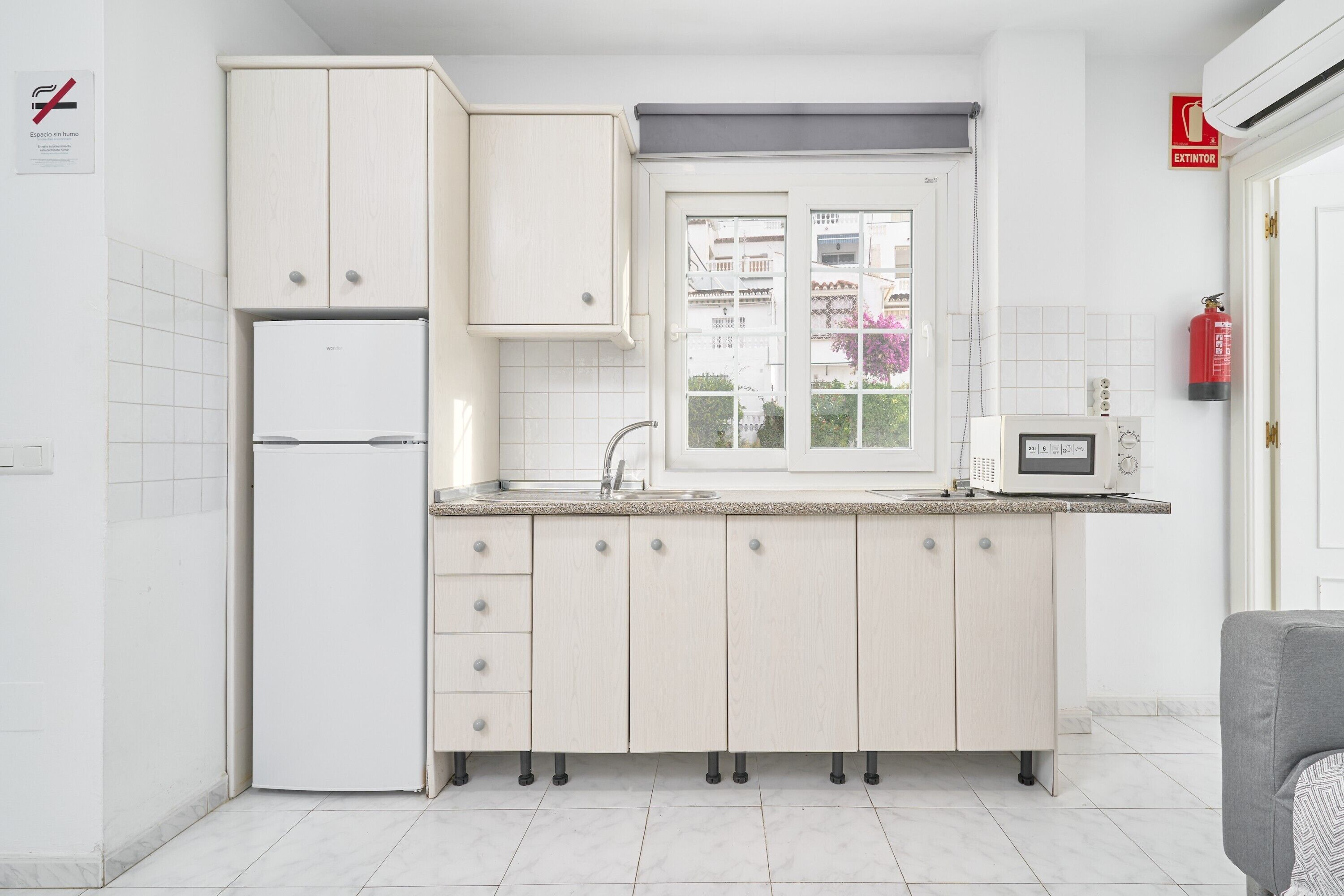A kitchen with white cabinets, a refrigerator, a microwave, and a window with a view of buildings.