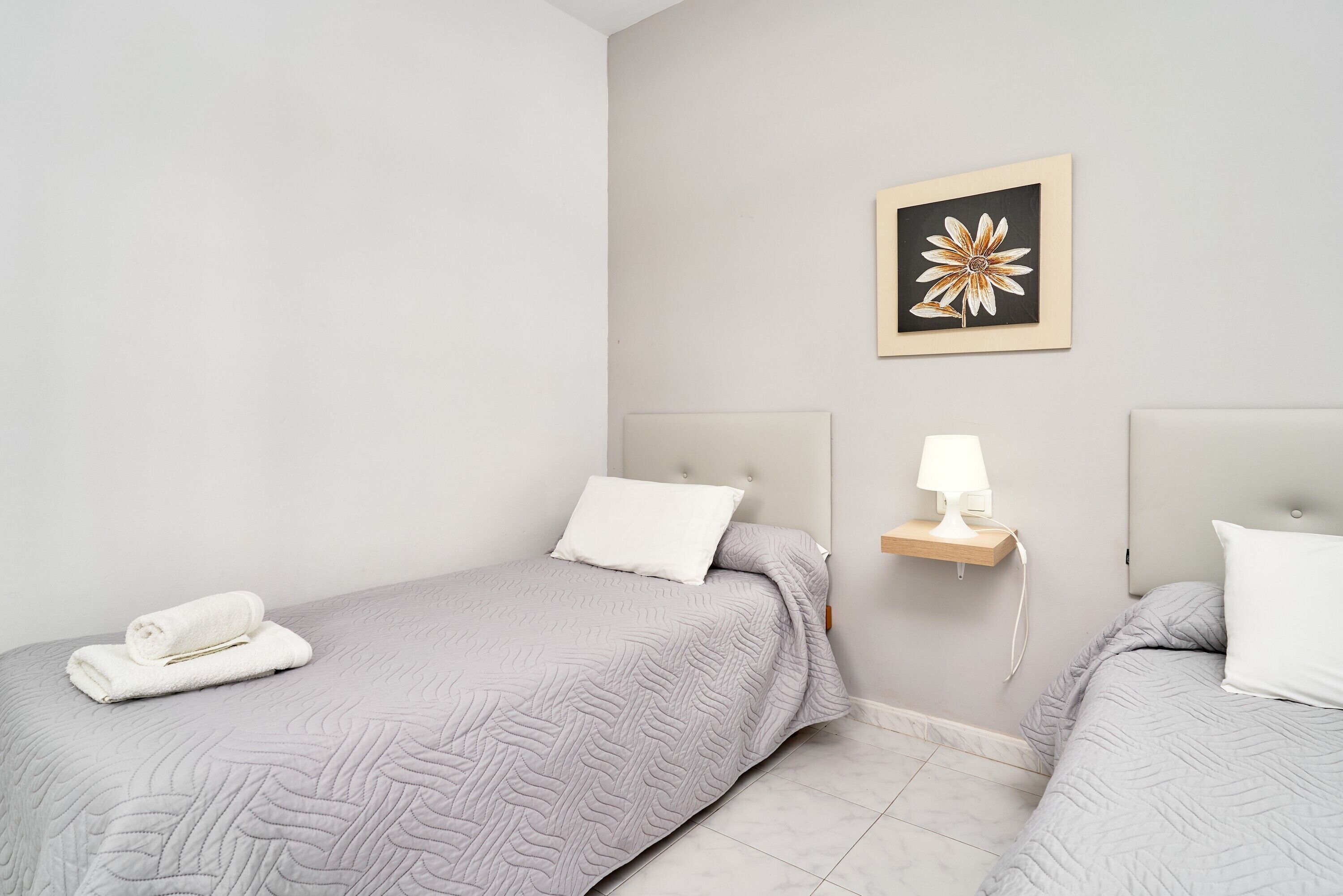 Ein Hotelzimmer mit zwei Betten, einem an der Wand hängenden Kunstwerk, einem Nachttisch mit Lampe und einem auf einem Bett liegenden zusammengerollten Handtuch.