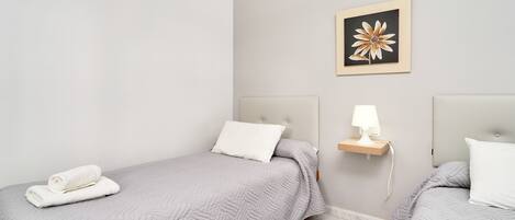 Ein Hotelzimmer mit zwei Betten, einem an der Wand hängenden Kunstwerk, einem Nachttisch mit Lampe und einem auf einem Bett liegenden zusammengerollten Handtuch.