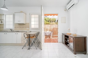 A kitchen with white cabinets, a dining table with chairs, an open door to a patio, and an air conditioning unit. - Apartment 'B-A' with Shared Pool, Wi-Fi and Air Conditioning (Nerja)