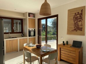 A modern kitchen with wooden cabinets, a built-in oven, and a dining area with a table set for two. - Charming 2-bedroom villa with AC in beautiful Sicilia (Sicilia)