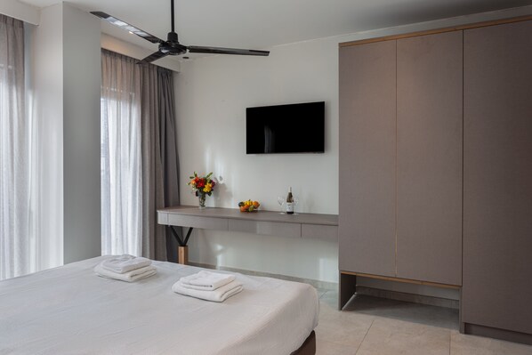 Une chambre d’hôtel moderne équipée d’un lit, d’un téléviseur à écran plat, d’un bureau agrémenté d’un vase de fleurs et d’une armoire.