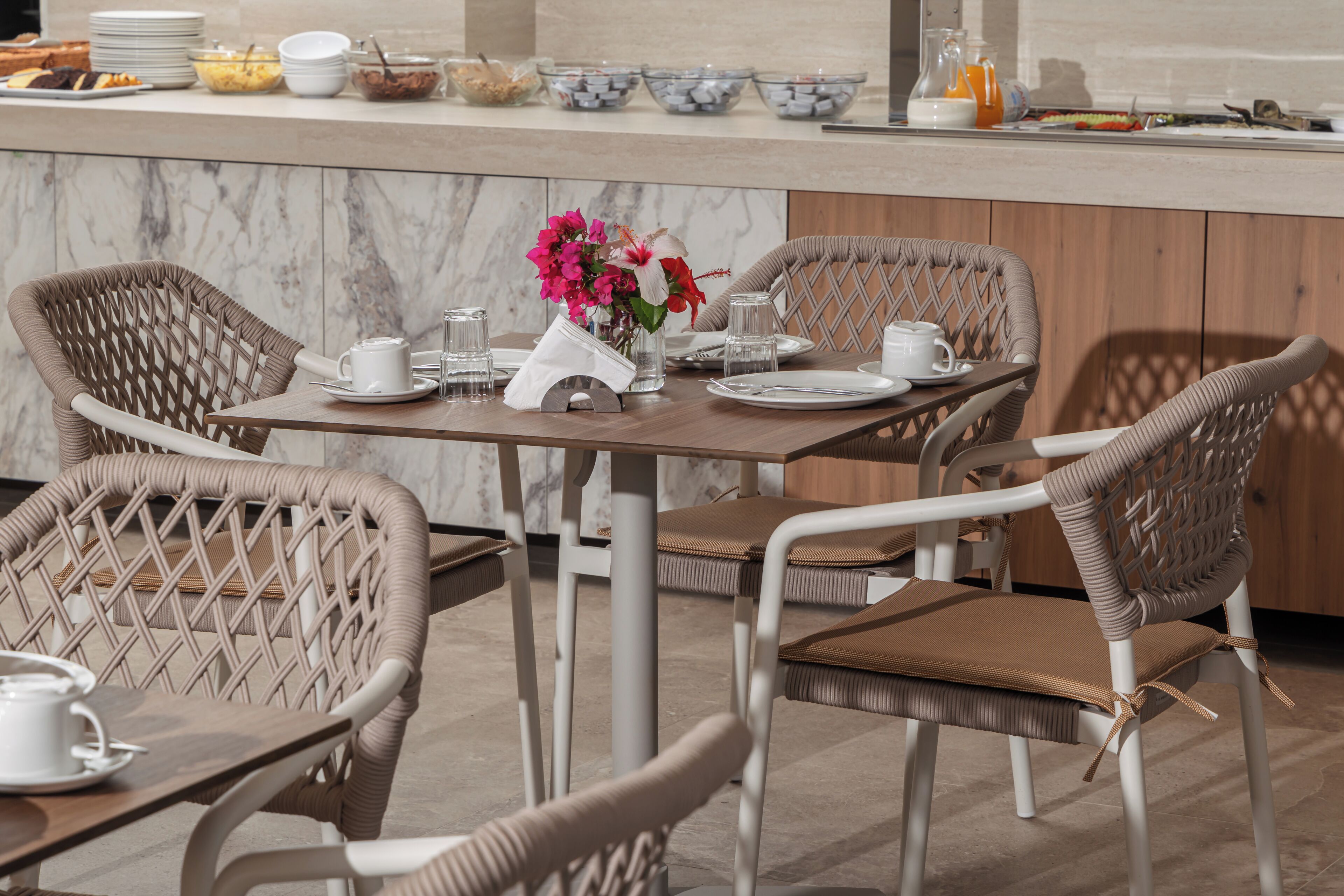 A dining area with wicker chairs, a marble countertop, and a vase with flowers.