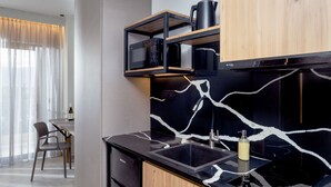 A modern kitchen with a black countertop, a built-in microwave, and a black and white marble backsplash. - Malia Odyssey Adults Only by Estia (Malia)