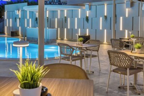 An outdoor seating area with a pool, lounge chairs, and tables. - Malia Odyssey Adults Only by Estia (Malia)