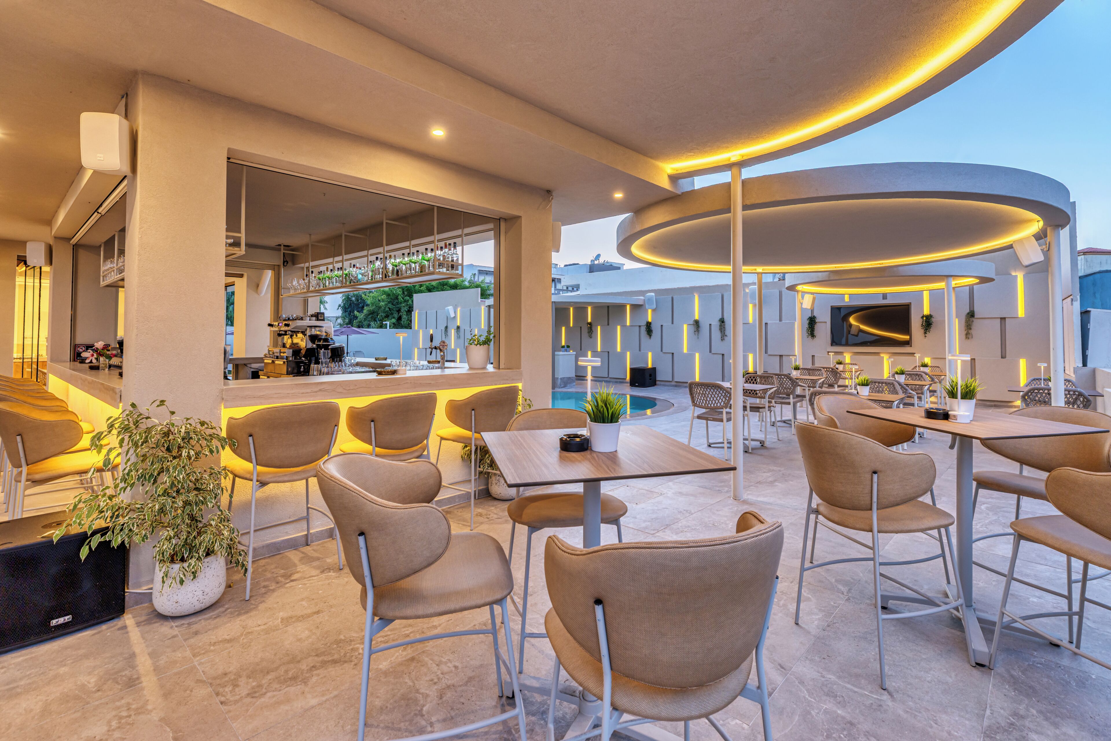 An outdoor seating area with tables and chairs, a bar, and a pool.