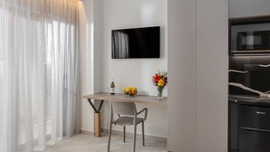 A modern kitchen with a built-in oven, a flat-screen TV, and a dining area with a chair and table. - Malia Odyssey Adults Only by Estia (Malia)