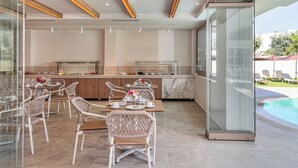 A modern outdoor dining area with wicker chairs, a marble countertop, and a glass enclosure overlooking a pool. - Malia Odyssey Adults Only by Estia (Malia)