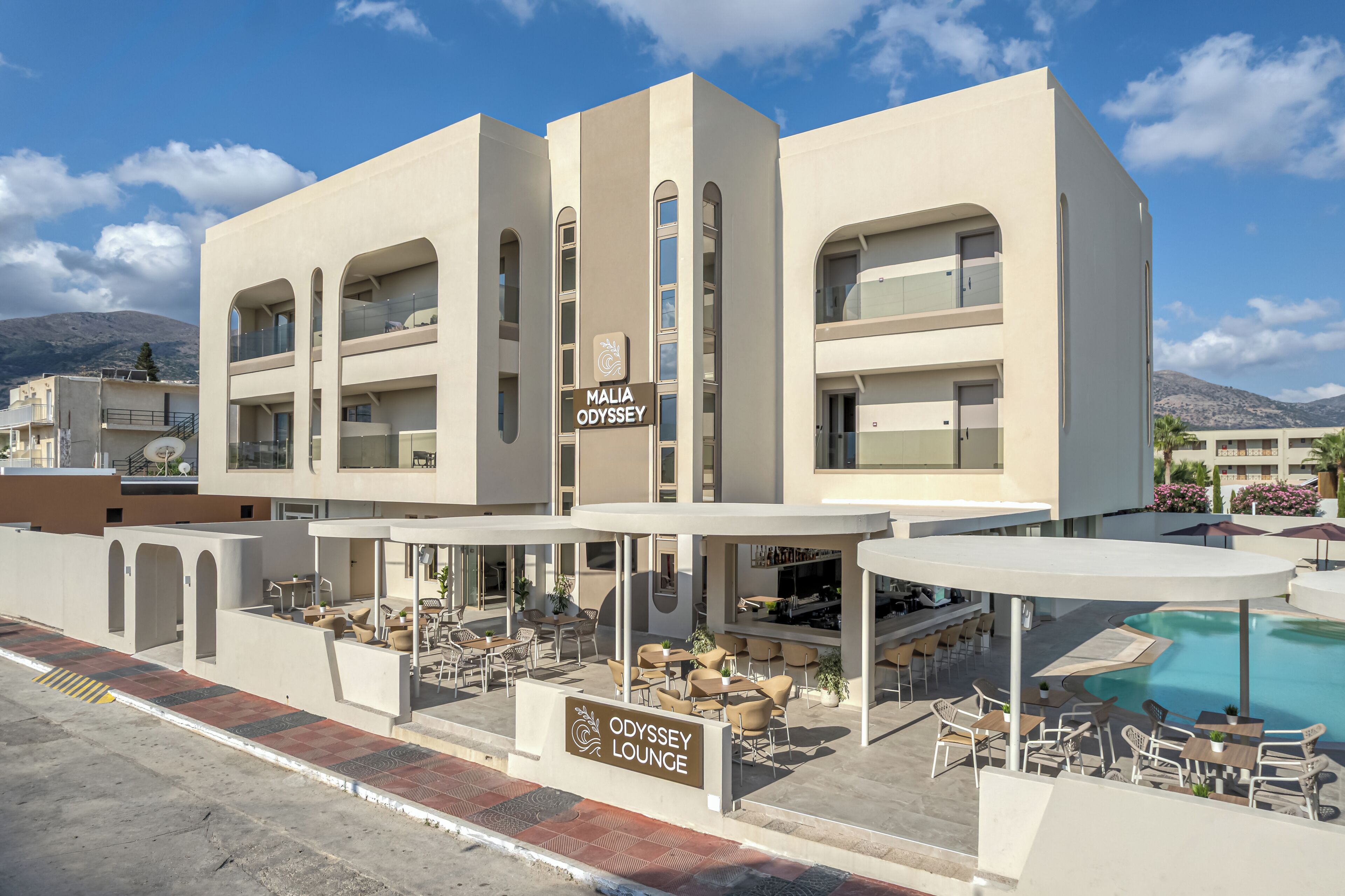Un hotel con piscina, mobiliario exterior y un letrero para el Odyssey Lounge.