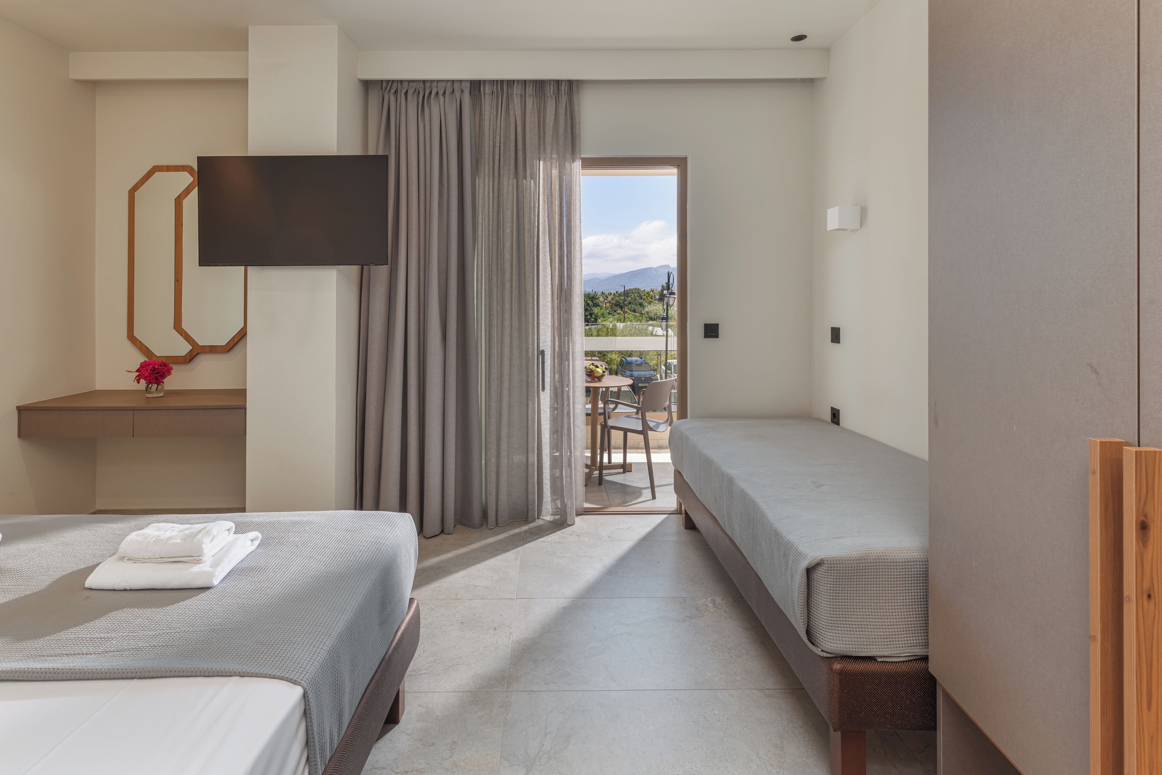 A hotel room with two beds, a TV, a desk, and a view of the outdoors.