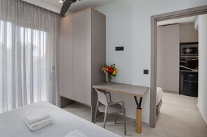 A modern hotel room with a bed, a desk, a chair, a vase with flowers, and a kitchenette. - Malia Odyssey Adults Only by Estia (Malia)