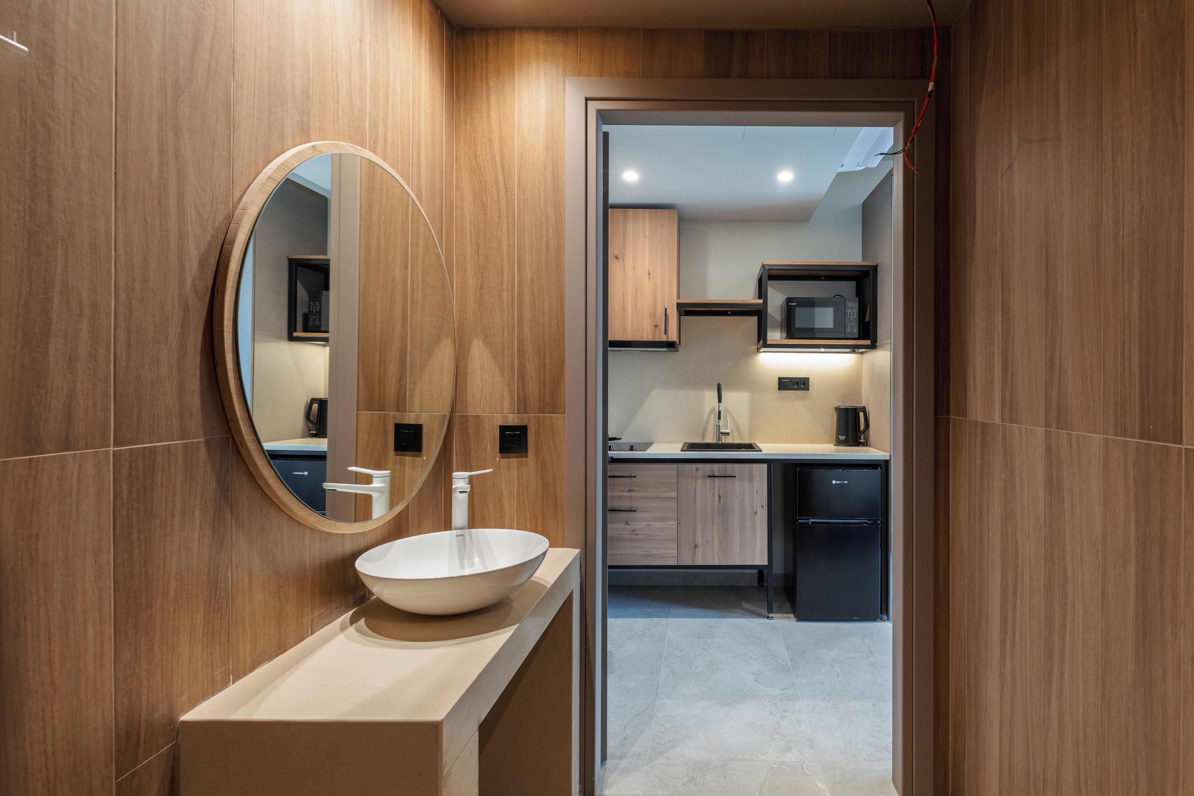 Un bagno moderno con uno specchio rotondo, un lavandino bianco e pannelli in legno.