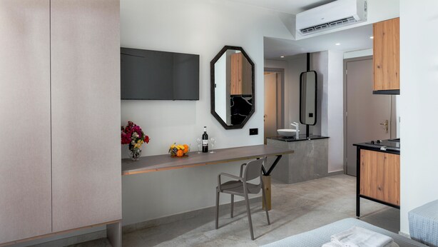 A modern hotel room with a bed, a desk, a chair, a large mirror, and a small bathroom area. - Malia Odyssey Adults Only by Estia (Malia)