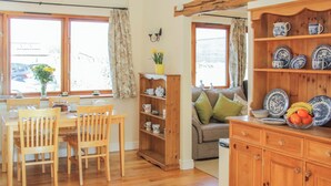 A cozy kitchen with wooden furniture, a dining table, and a sofa. There are shelves with dishes and a vase with flowers. - Herdwick Cottage (Much Wenlock)