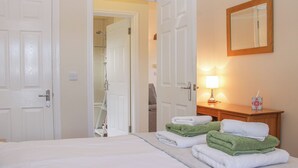 A hotel room with a bed, a wooden nightstand, a mirror, and a bathroom visible through an open door. - Herdwick Cottage (Much Wenlock)