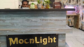 A reception desk with a sign reading 'MocnlLight,' a large screen displaying a green and yellow image, and a ceiling fan. - Hotel Moon Light Indore (Indore)