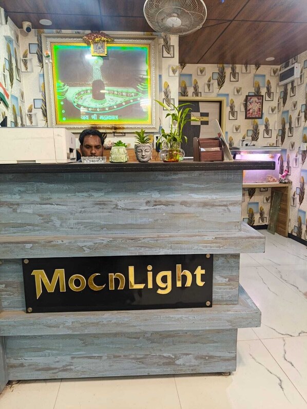 A reception desk with a sign reading 'MocnlLight,' a large screen displaying a green and yellow image, and a ceiling fan.